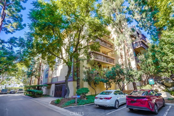 Front view of a multi-story residential building with balconies and surrounding trees.