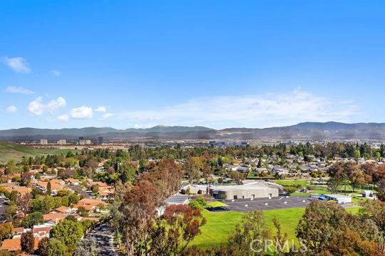 Aerial view of a suburban area with residential buildings, greenery, and distant mountains.