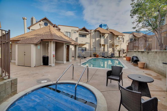 Outdoor swimming pool area with surrounding residential buildings and a small round hot tub.