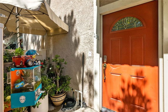 Partial view of the front entrance of a house with an orange door and plants.