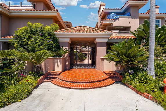 Front view of a two-story house with terracotta roof tiles and brick steps leading to a gated entrance.