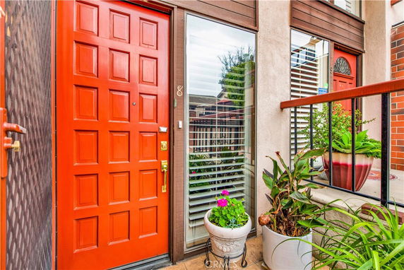 Front view of a house entrance with a red door and large glass window with plants.