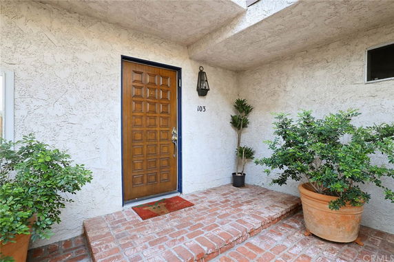 Front entrance of a house with a wooden door and potted plants on a brick porch.