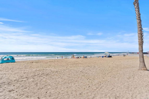 Sandy beach with people and umbrellas, and a blue ocean in the background.