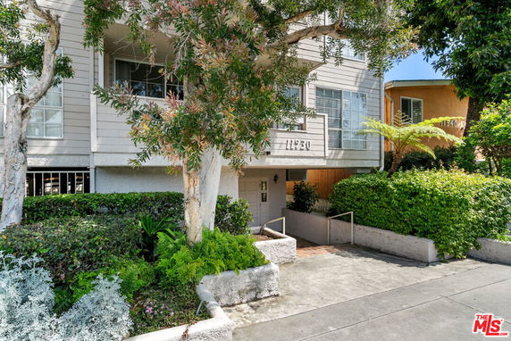 Front view of a multi-story residential building with trees and shrubs.
