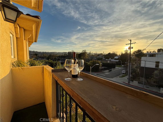 Panoramic view from a balcony at sunset with a wine bottle and glasses on a railing overlooking neighboring buildings and streets.