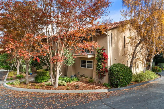 Front view of a two-story house with a balcony and autumn foliage.