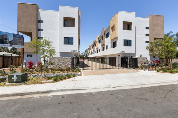 Front view of a multi-story modern apartment building with gated entrance.