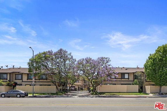 Front view of a two-story residential building with trees and a fence.