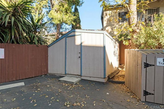Outdoor view of a small storage shed with a slanted roof, surrounded by a wooden fence.