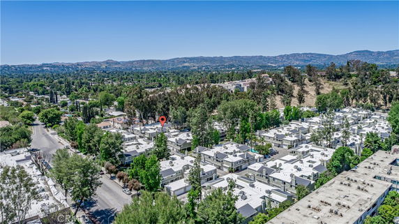 Aerial view of a residential area with multiple buildings and trees surrounded by hills and greenery.