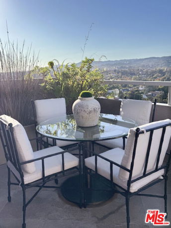 Outdoor seating area with a round glass table and cushioned chairs, offering a scenic view of the surroundings.