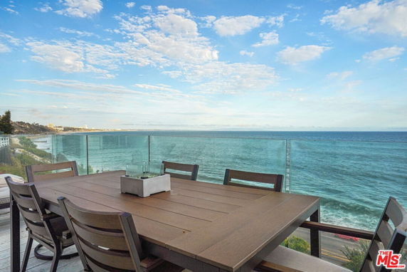 Wide angle view from a balcony overlooking the ocean with a dining table and chairs.