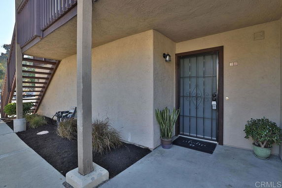 Front view of a ground-level entry with stairs leading to an upper level and potted plants by the door.