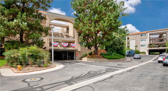 Front view of a multi-story residential building with parking spaces and trees.