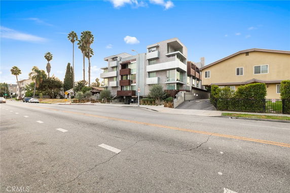 Front view of a modern multi-story residential building with balconies and a driveway.