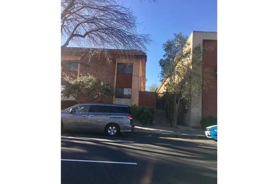 Front view of a multi-story brick building with trees and parked cars in front.
