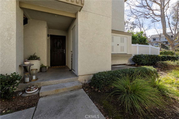 Front entrance view of a residential building with plants and steps leading to a door.