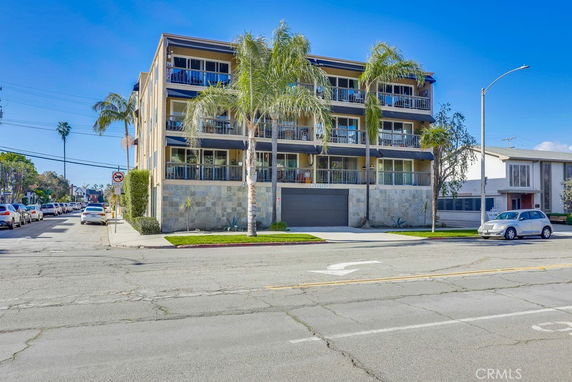 Front view of a multi-story residential building with balconies and palm trees.