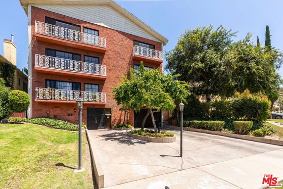 Front view of a three-story brick building with balconies and driveway.