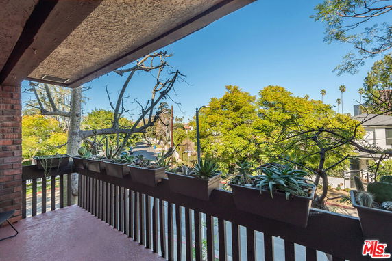 View of surrounding trees and buildings from a balcony with potted plants.
