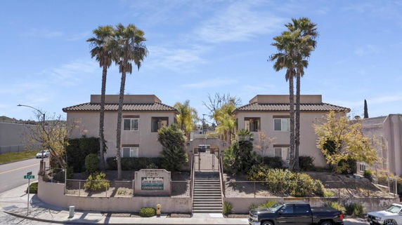 Front view of a two-story condominium complex with gated entrance and palm trees.