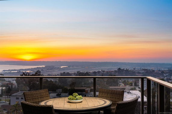 Panoramic view of sunset over a cityscape with an outdoor table and chairs on a balcony.