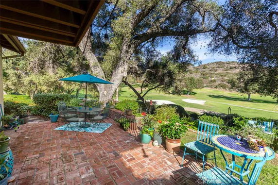 Outdoor seating area with brick flooring and a view of a golf course and hills.