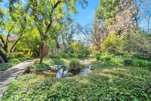 View of a garden area with trees, a path, and a small pond.