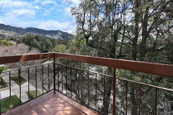 Panoramic view from a balcony showcasing trees and distant hills.