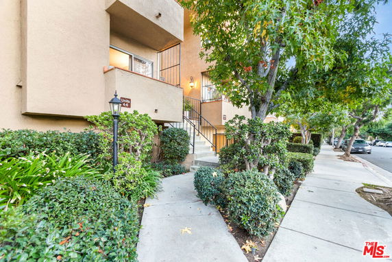 Front view of a multi-unit building entrance with stairs and surrounding greenery.