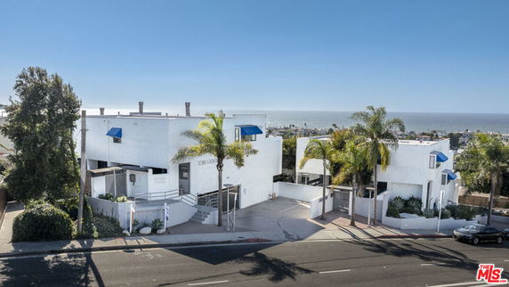 Front view of a white multi-story building with blue awnings and a driveway.