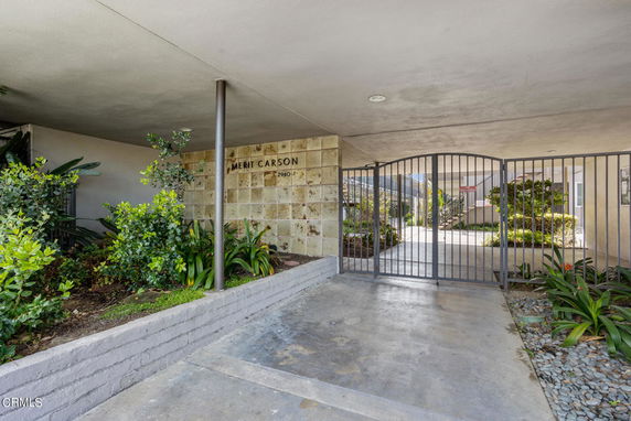Entrance view of a gated residential building with stone wall and covered pathway.