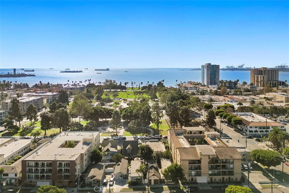 Aerial view of a coastal cityscape with buildings, greenery, and ocean in the background.