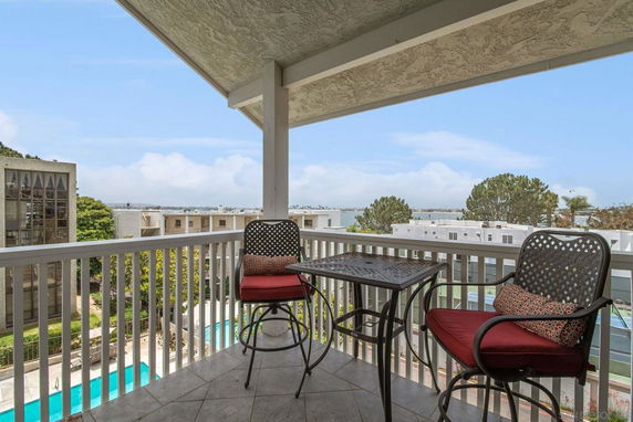 Panoramic view from a balcony with chairs overlooking a cityscape and swimming pool.