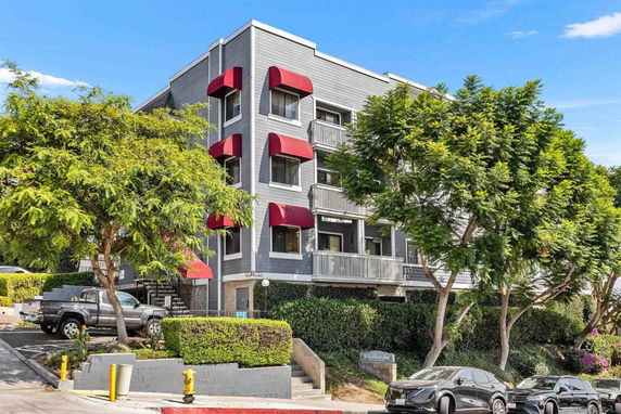 Front view of a multi-story building with red awnings and balconies.