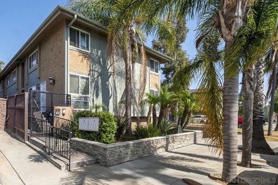 Front view of a two-story residential building with palm trees and a gated entrance.