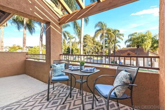 A veranda with outdoor seating overlooking palm trees and a nearby building.