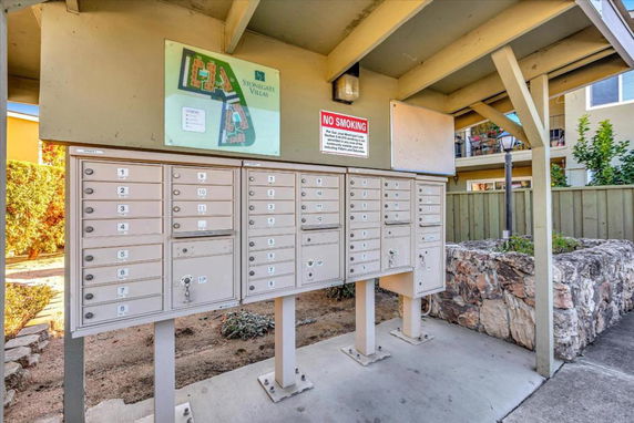 Outdoor group mailboxes on a covered concrete area with a building map and no smoking sign.