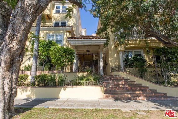 Front view of a multi-story house with stairs and a gated entrance.