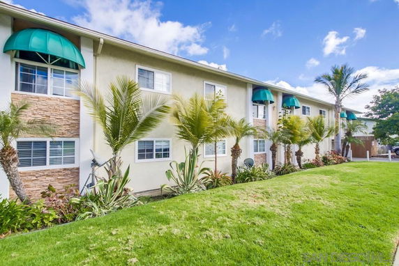 Front view of a two-story residential building with green awnings and palm trees.