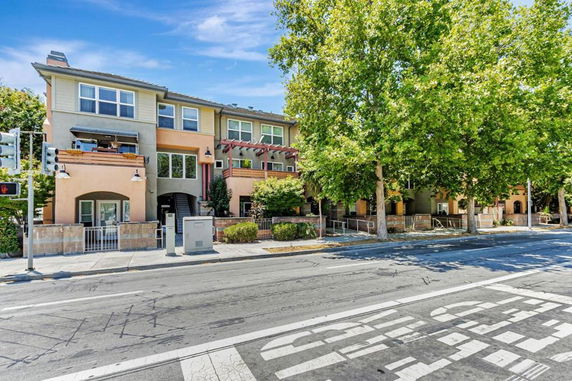 Front view of a multi-story townhouse with balconies and trees lining the street.