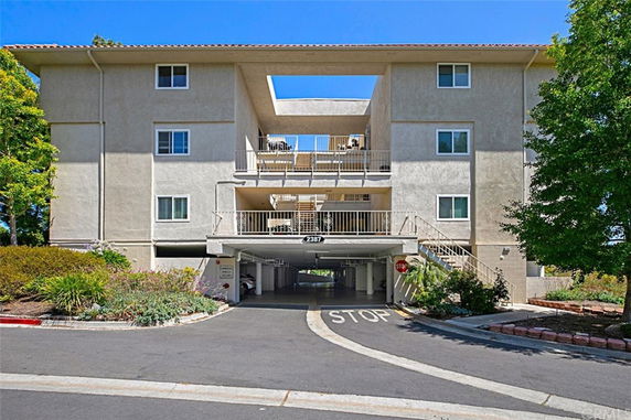 Front view of a multi-story residential building with an open parking area at the ground level.