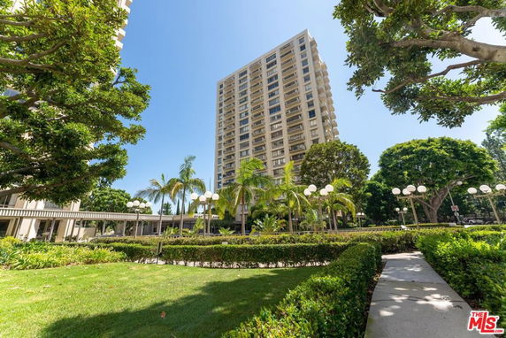 View of a high-rise building with multiple balconies, surrounded by trees and landscaped areas.