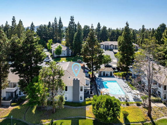 Aerial view of residential buildings surrounded by tall trees with a swimming pool in the center.