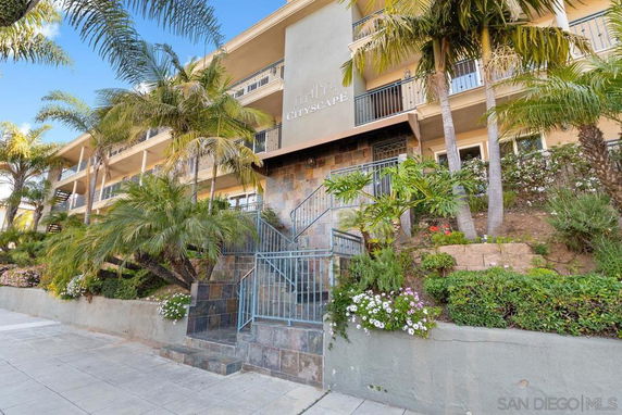 Front view of a multi-story building with balconies and landscaped entrance.
