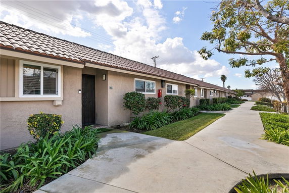 Front view of a row of single-story townhouses with tiled roofs and landscaped pathways.