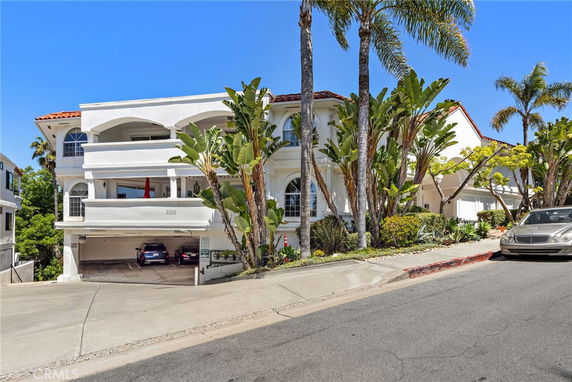 Front view of a three-story house with a covered parking area on a sloped driveway.