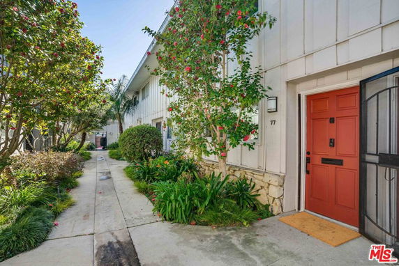Front view of a building entrance with a red door and surrounding greenery.