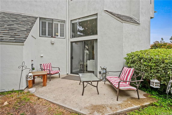 Outdoor view of a multi-story building with sliding glass doors and windows, leading to a small patio area with chairs and a table.